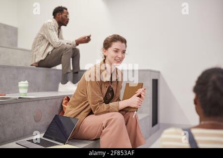 Side view portrait of young female student chatting with friends while relaxing in modern school lounge, copy space Stock Photo