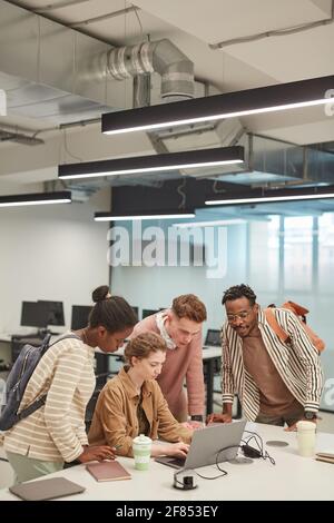 Vertical wide angle shot of diverse group of young students using laptop together while working on school project in college, copy space Stock Photo