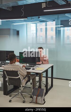Vertical full length of IT programmers or students using computers in office interior with glass wall, copy space Stock Photo