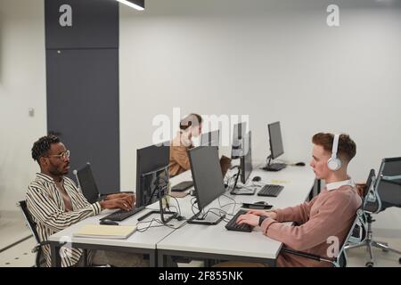 Wide angle view at group of young people using computers while working in office or school IT lab, copy space Stock Photo