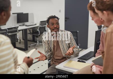 Portrait of African-American man talking to colleagues in office and gesturing actively while collaborating on project Stock Photo