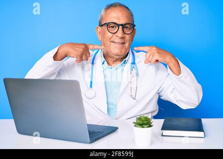 Senior handsome man with gray hair wearing doctor uniform working using computer laptop smiling cheerful showing and pointing with fingers teeth and m Stock Photo