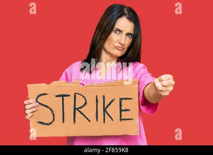 Middle age brunette doctor woman holding strike banner cardboard annoyed and frustrated shouting with anger, yelling crazy with anger and hand raised Stock Photo