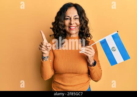 Middle age hispanic woman holding el salvador flag smiling happy pointing with hand and finger to the side Stock Photo