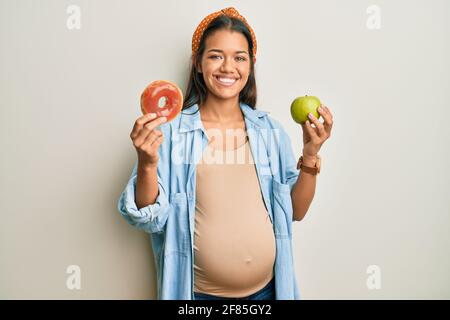Beautiful hispanic woman expecting a baby, holding food smiling with a happy and cool smile on face. showing teeth. Stock Photo