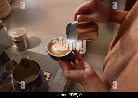 Close up of unrecognizable barista creating latte art with cream while making fresh coffee in cafe or coffee shop, copy space Stock Photo