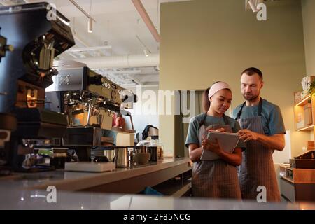 Waist up portrait of two young waiters wearing aprons while doing inventory in cafe or coffee shop, copy space Stock Photo