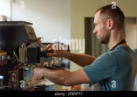 Side view portrait of male barista making fresh coffee in cafe and operating coffee machine Stock Photo