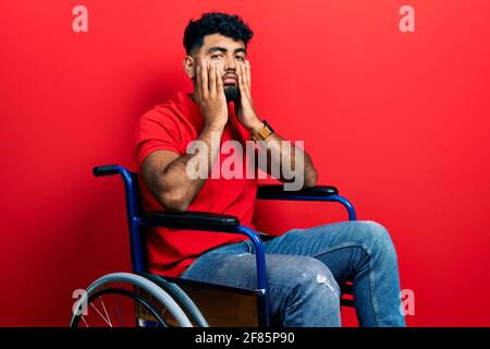 Arab man with beard sitting on wheelchair tired hands covering face, depression and sadness, upset and irritated for problem Stock Photo