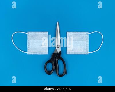 Medical disposable face mask cut in half and scissors on a blue background. Stock Photo