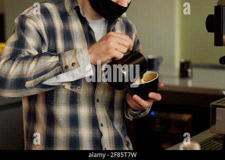 Cropped shot of male barista making fresh coffee with cream while working at bar in cafe or coffee shop Stock Photo