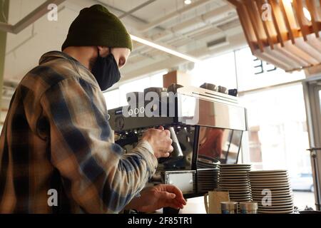 Side view at male barista using coffee machine while making fresh coffee at bar in cafe, copy space Stock Photo