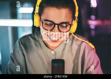 Smiling attractive young woman in glasses and headphones recording podcast Stock Photo