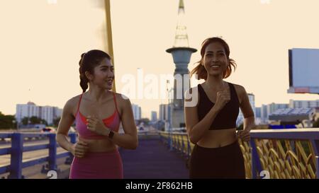 Two healthy and fit young female friends jogging on city street during early morning while talking and smiling in city Stock Photo
