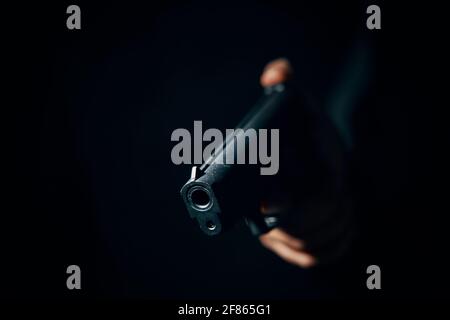 Close-up of black gun in hand on dark background. Firearms in shadows. Crime or defense. Dangerous pistol in hand. Copy space. Stock Photo