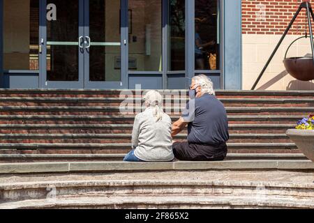 Frederick , Maryland, USA 04-07-2021: A senior caucasian couple are sitting in a park holding hands during COVID-19 pandemic. They both wear face mask Stock Photo