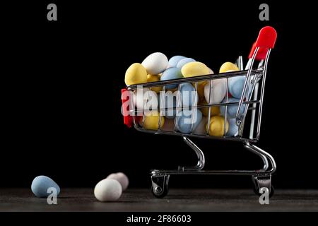 Dark background image with a toy shopping cart filled with crisp sugar coated chocolate egg A concept image for holiday shopping for christmas or east Stock Photo
