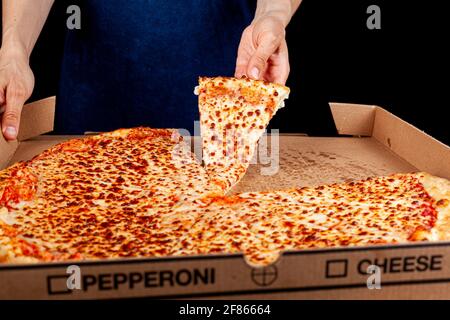 Close up top image of a caucasian woman holding a slice of fresh cheese pizza with a large pizza in carboard box in background. Concept image for fast Stock Photo