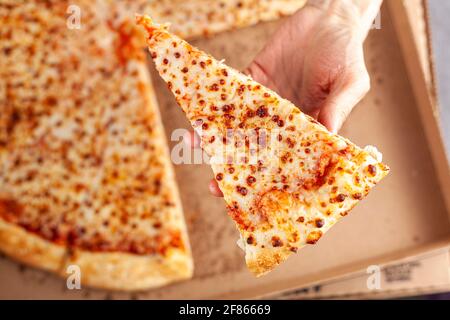 Close up flat lay image of a caucasian woman holding a slice of fresh cheese pizza with a large pizza in carboard box in background. Concept image for Stock Photo