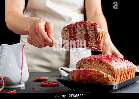 Closeup image of fresh homemade blood orange cake made in a loaf pan and served on black porcelain plate on dark stone background.  It has blood orang Stock Photo