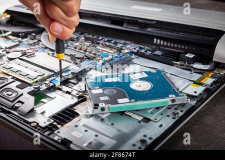A computer technician is repairing an old laptop using a screw driver. Closeup isolated image showing complex interior of a laptop with circuit boards Stock Photo