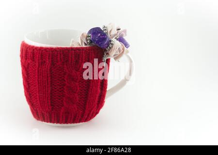 White mug with red knitted sweater covering with purple gem and shell bracelet on white background isolated Stock Photo