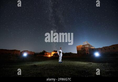 Young spaceman in special white space suit standing and looking on starry sky with Milky way at night. Stock Photo