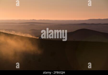 A 4x4 leaves a trail of dust in the sun as it climbs a mountain dirt track. Stock Photo