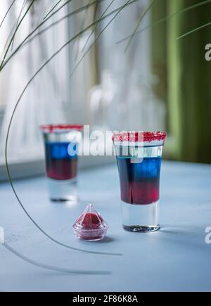Two shots of Fourth of July alcohol cocktail on blue textured table. Bright red, blue and white layered cocktails in small glasses for USA Independenc Stock Photo