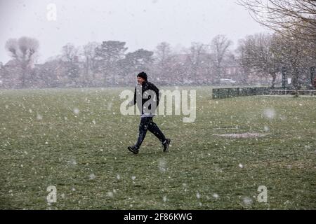 London, UK. April 12 2021: A jogger makes his way through a snow blizzard inside Dundonald Park of South Wimbledon on the first day the coronavirus restrictions are lifted in England to enable people to get their haircut and eat & drink outside pubs and restaurants. April 12th 2021 Wimbledon, England. Credit: Jeff Gilbert/Alamy Live News Stock Photo