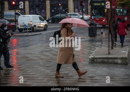 London, UK. April 12 2021: Commuters make their way to work through a surprising Spring snow blizzard in Wimbledon on the first day the coronavirus restrictions are lifted in England to enable people to get their haircut and eat & drink outside pubs and restaurants. April 12th, Wimbledon, Southwest London SW19, England, UK Credit: Jeff Gilbert/Alamy Live News Stock Photo