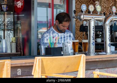 Man bartender behind bar. Sunny autumn day. Side view. Crimea, Sudak - 10 October 2020. Stock Photo