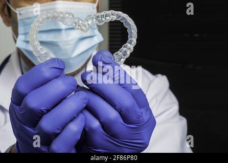 Caucasian dentist holding an orthodontic transparent dental aligners forming a heart shape Stock Photo