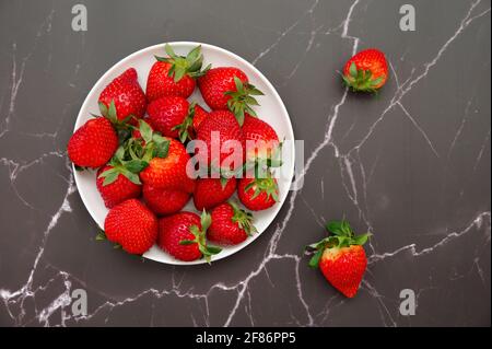 Flat lay of strawberries on a plate against black marble background Stock Photo