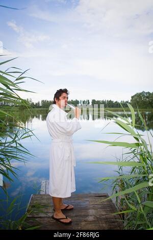 Man in bathrobe brushing teeth at tranquil lake Stock Photo