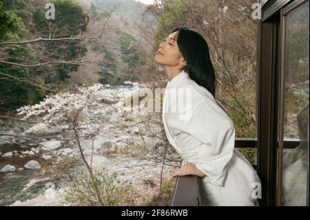 Beautiful carefree young woman in bathrobe on balcony overlooking river Stock Photo