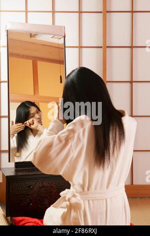 Young woman in bathrobe combing hair at mirror in spa Stock Photo