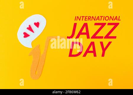 A cutted out of felt saxophone from which hearts flew out, on a yellow background. Flat lay. International Jazz Day. Stock Photo