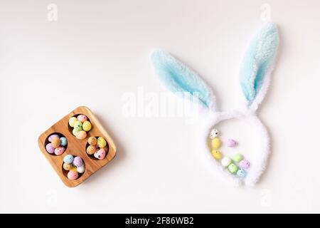 Bunny ears and colored little eggs on white background on Easter day. Top view. Symbol Happy Easter holiday concept. Flat lay. Copy space. Stock Photo