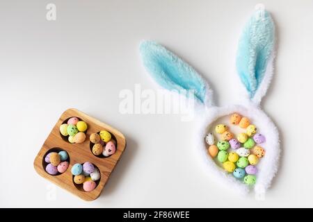 Bunny ears and colored little eggs on white background on Easter day. Top view. Symbol Happy Easter holiday concept. Flat lay. Copy space. Stock Photo