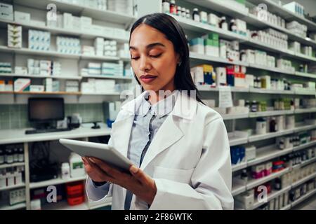 Young female pharmacist working using digital tablet standing in chemist wearing labcoat Stock Photo