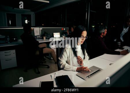 Female employee busy in her work on laptop in office and with colleagues at background Stock Photo