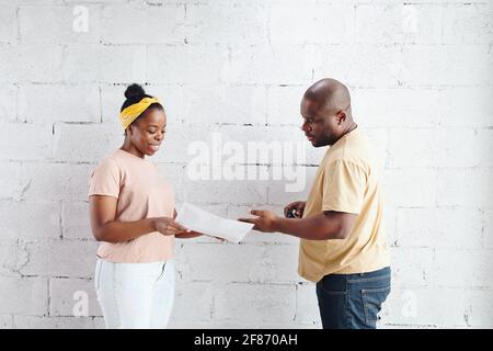 Young smiling African woman showing paper with photo of living-room interior to her husband while consulting about some moments Stock Photo