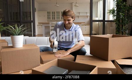Smiling man packing cardboard boxes at home, using adhesive tape Stock Photo