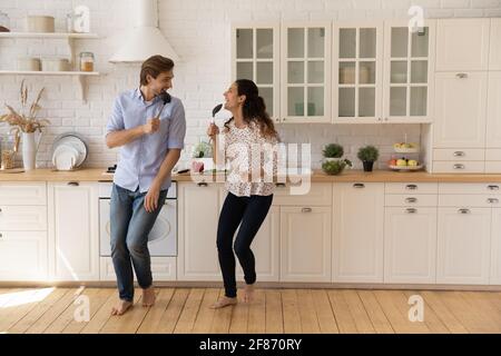 Overjoyed young couple singing into kitchenware, dancing in kitchen Stock Photo