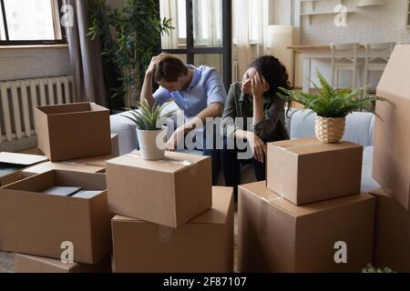 Unhappy frustrated couple sitting on couch with cardboard boxes, eviction Stock Photo