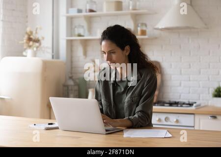 Confident focused woman using laptop, working online in kitchen Stock Photo