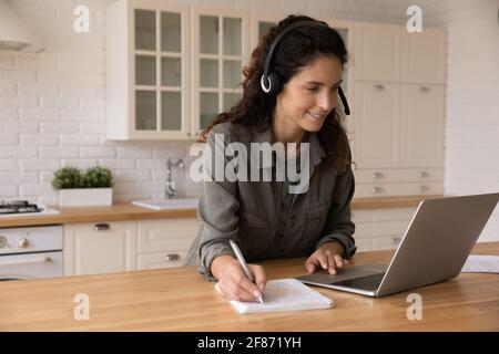 Close up smiling woman in headphones using laptop, taking notes Stock Photo