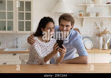 Happy young family looking at smartphone screen, sitting in kitchen Stock Photo