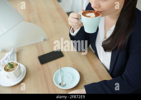 Cropped image of young businesswoman drinking cup of latte at cafe table Stock Photo